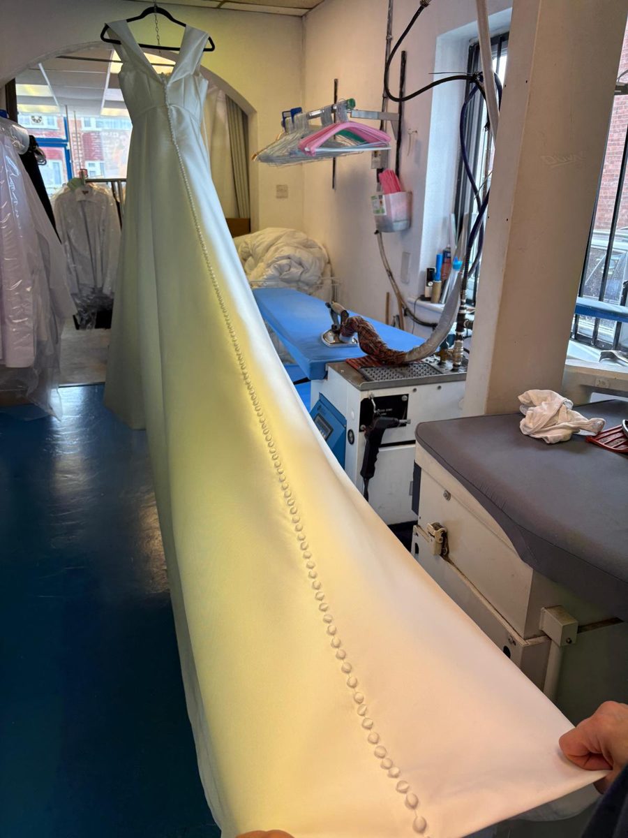An ivory wedding gown with a long buttoned train being pressed in the workroom