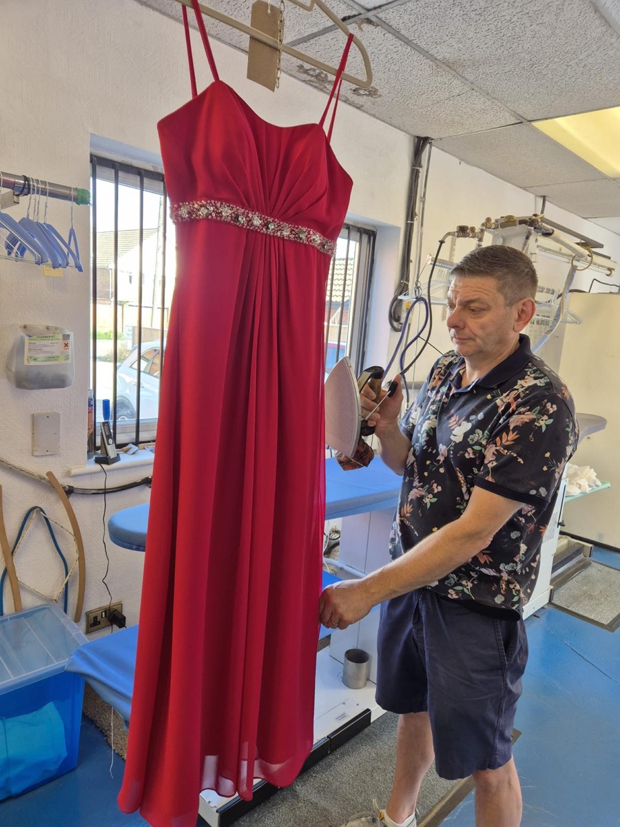 Paul steaming and pressing a red evening gown inside the Tudor Dry Cleaners workroom