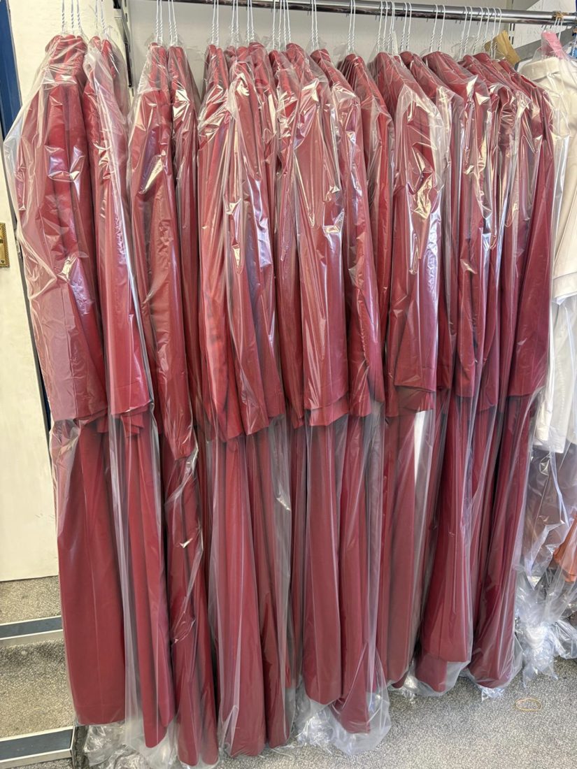 A full rail of red gowns freshly cleaned and covered in protective covers, ready to collect